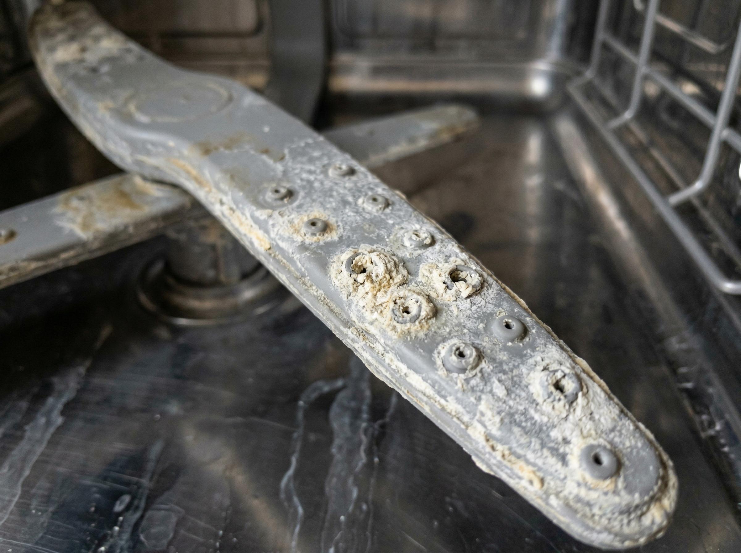 Macro close-up of a dishwasher spray arm with calcium scale buildup clogging the jets